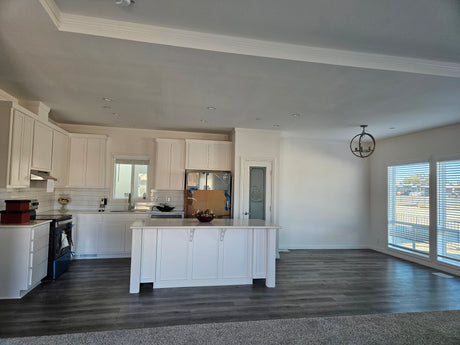 Modern kitchen with white cabinets and island, large windows, and gray flooring.